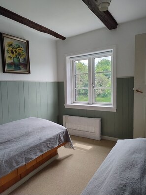 A room with two beds, a radiator, a window with a view of greenery, and a painting on the wall. - Cosy holiday apartment on Bornholm (Hollændergårde)