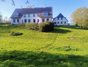Une grande maison à deux étages, dotée d’un toit en pente, entourée d’une pelouse bien entretenue et d’un petit jardin.