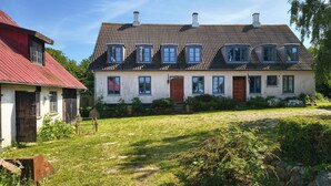 A two-story house with a sloped roof, multiple windows, and a small garden area with grass and rocks. - Cosy holiday apartment on Bornholm (Hollændergårde)
