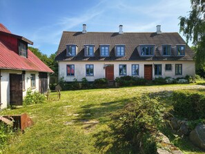 Ein zweigeschossiges Haus mit geneigtem Dach, zahlreichen Fenstern und einem kleinen Garten mit Gras und Steinen.