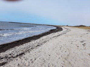 Ein Sandstrand mit felsiger Küste und einem Steg, der sich ins Wasser erstreckt.