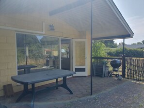 Een terras met een tafel en stoelen, een barbecue en een overdekte zithoek.