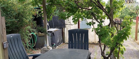Un espacio de estar al aire libre cubierto, con una mesa y sillas, rodeado de follaje y una pérgola.
