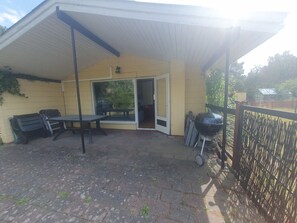 Ein überdachter Patio-Bereich mit Tisch und Stühlen, einem Grill und einer Glastür, die in einen Innenraum führt.
