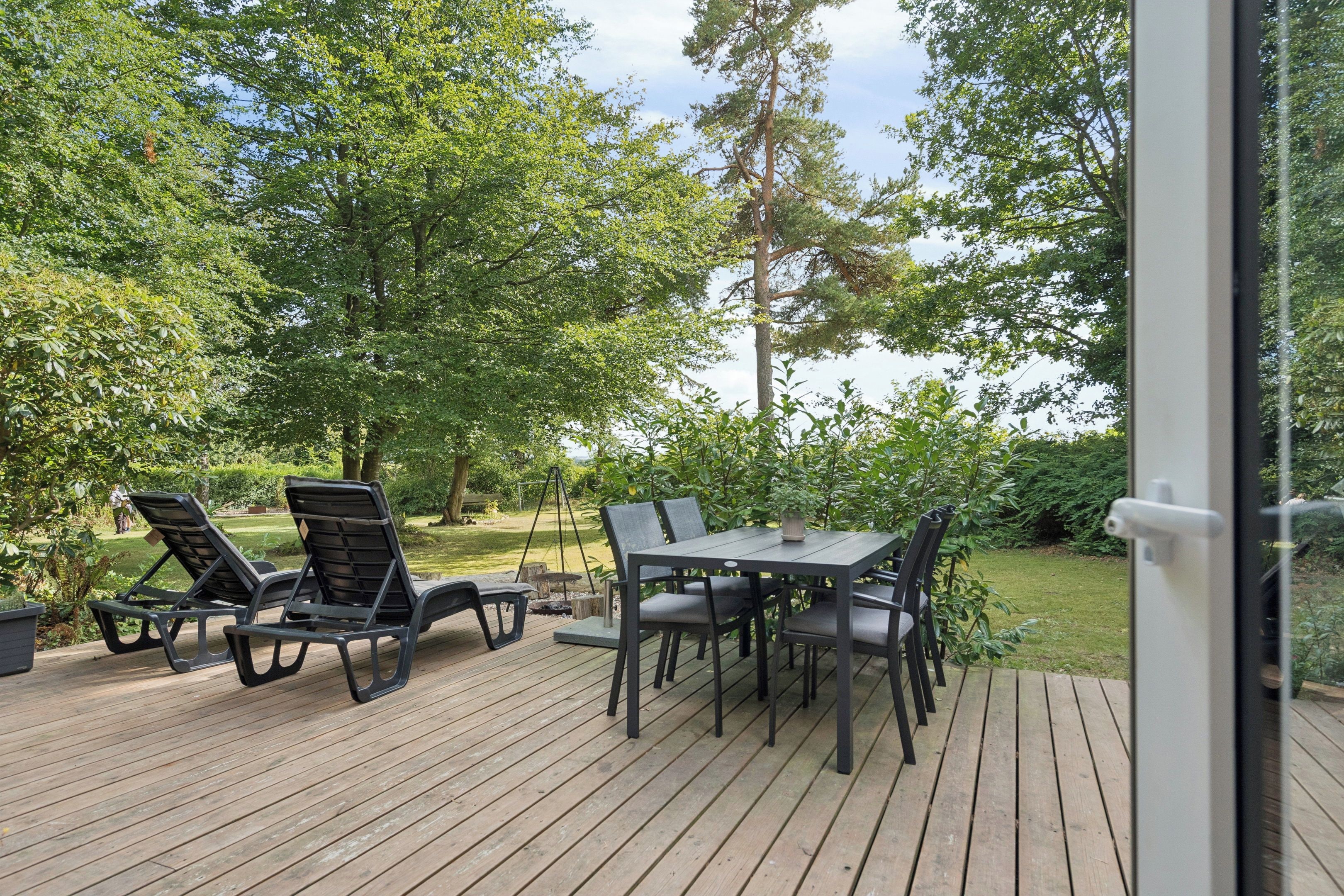 Een terras buiten met een tafel en stoelen, omgeven door weelderig groen en bomen.