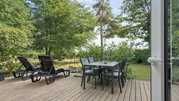 Een terras buiten met een tafel en stoelen, omgeven door weelderig groen en bomen.