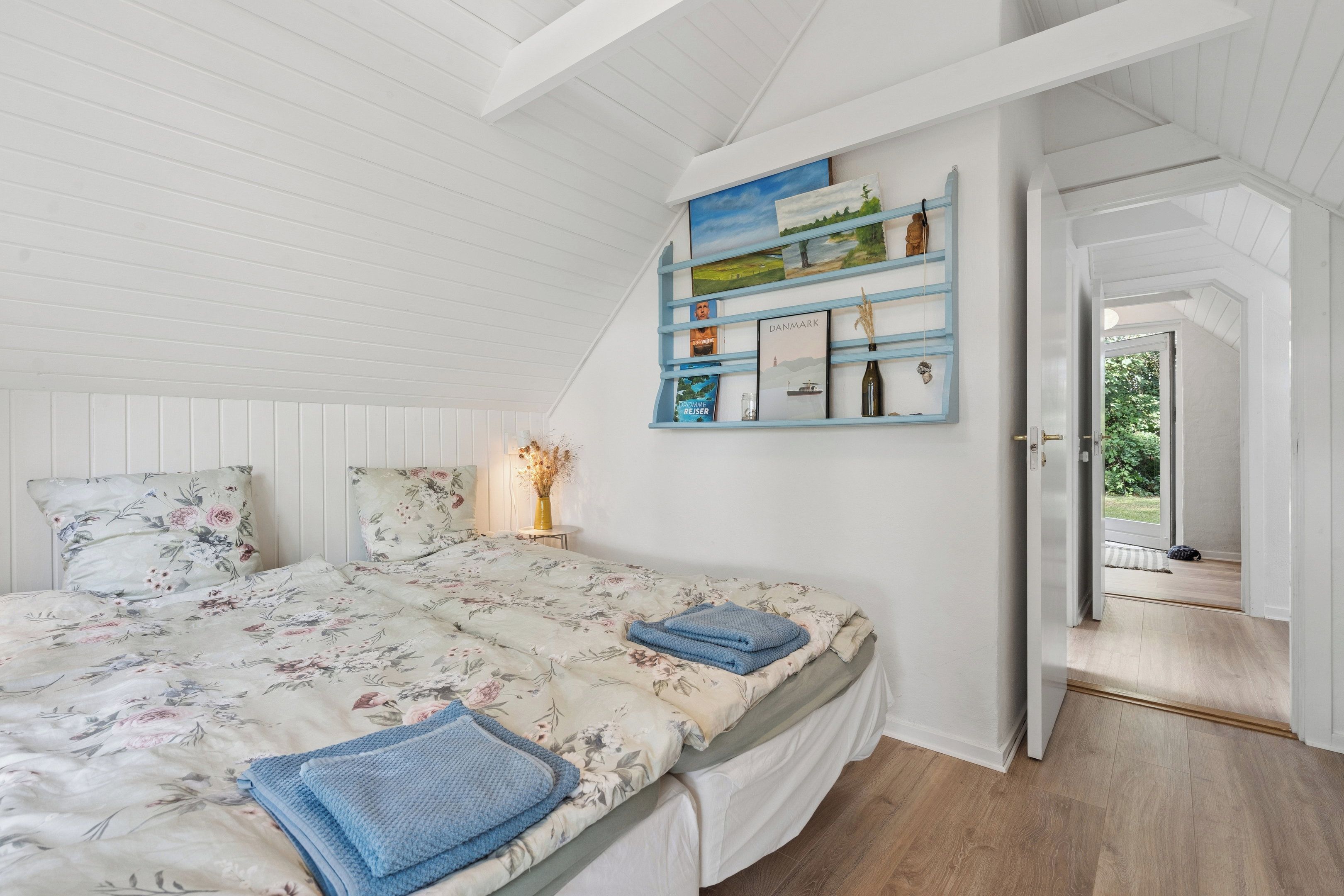 Une chambre à coucher comprenant un lit, des oreillers, une table de chevet, une étagère murale avec des livres et des objets décoratifs, et une porte donnant sur un espace extérieur.