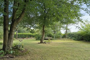 Een gazon met bomen, een bankje en een voetbalkooi.