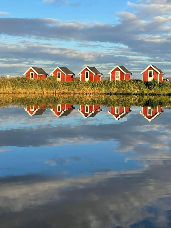 A row of red buildings with a clear reflection in calm water.