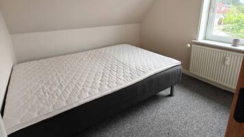 A small, sloped ceiling room with a single bed, a window, and a radiator.