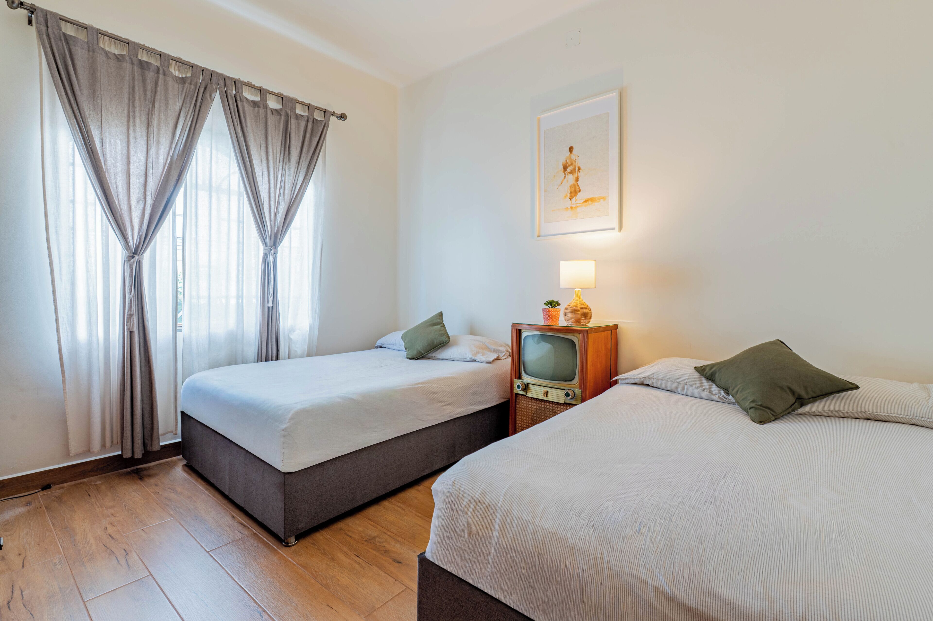 A hotel room with two single beds, a television, and a painting on the wall.