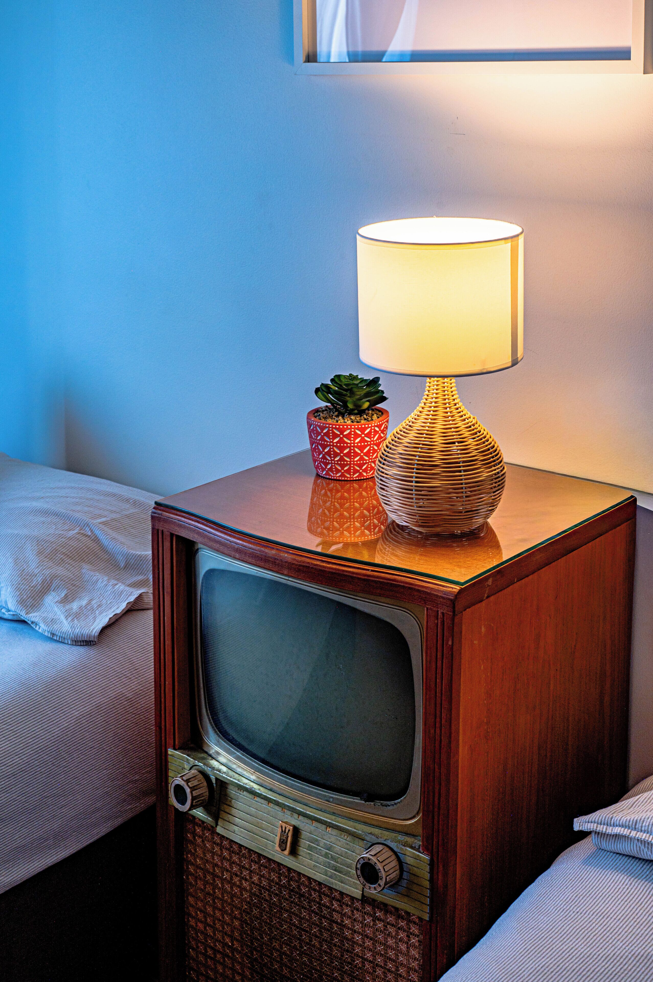 Un téléviseur ancien posé sur une table de chevet en bois, avec une lampe et une plante en pot.