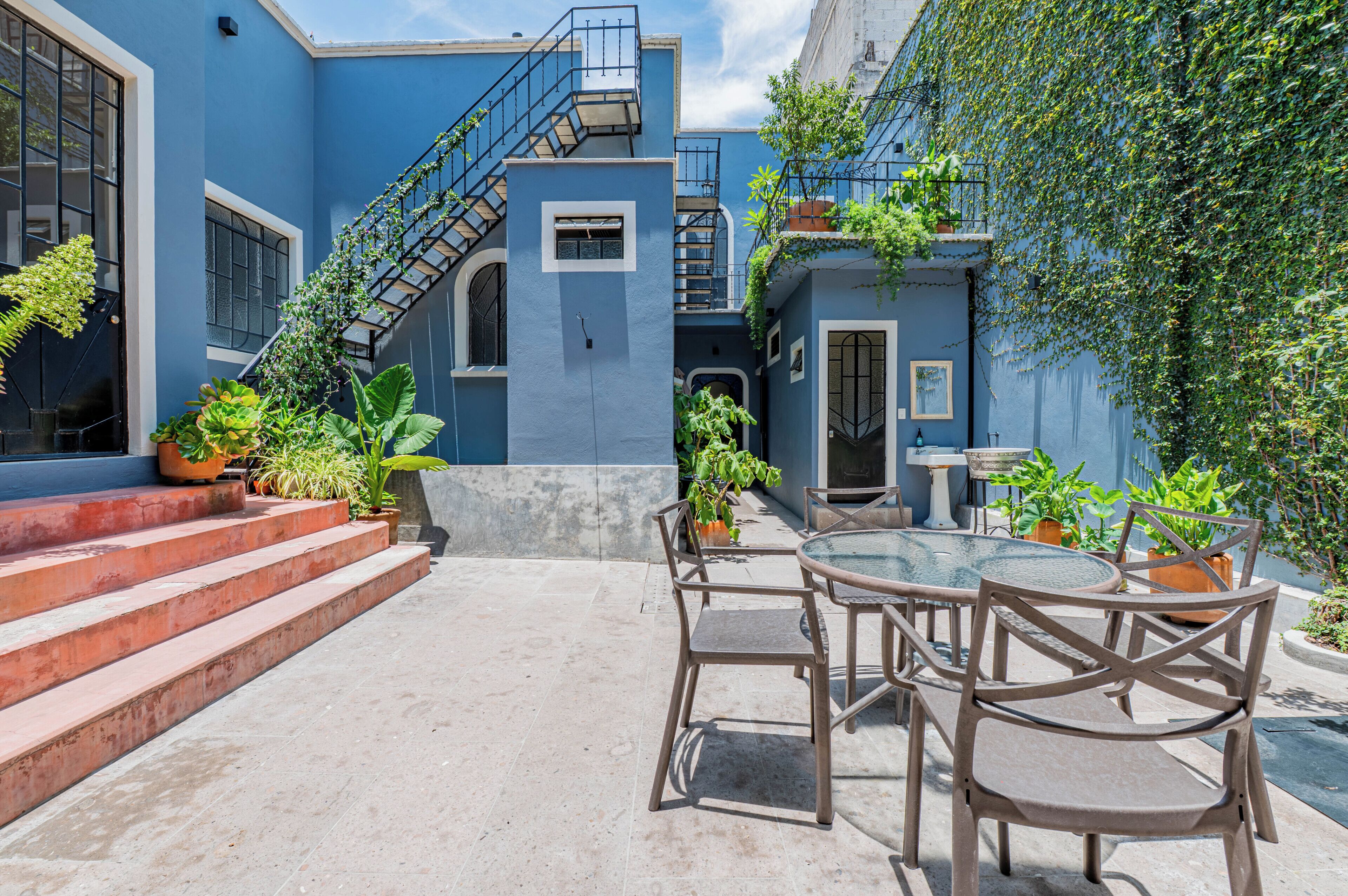 A courtyard with a blue building, a staircase, and outdoor seating with chairs and tables.