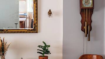 A dining area with a table set for two, a mirror, a potted plant, and a grandfather clock.