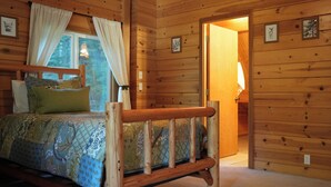 Un dormitorio de cabaña de madera con cama, cortinas y ventana.