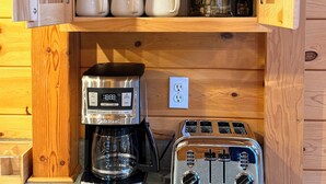 Un mueble de madera con cafetera, tostadora y tazas y vasos apilados.