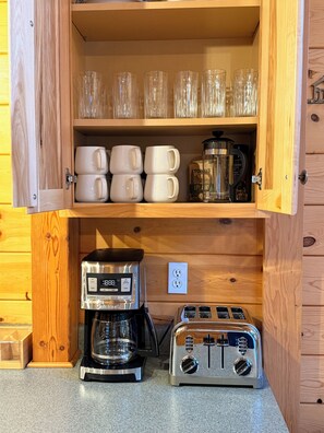 A wooden cabinet with a coffee maker, toaster, and stacked cups and mugs. - Charming Log Cabin Tucked Away Near Cle Elum (Cle Elum)