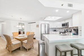 A modern kitchen with white cabinetry, a stainless steel refrigerator, and a large island with bar stools. - Ocean View Retreat at Beach Palms (Indian Shores)