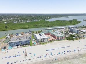 Un hôtel situé sur la côte, composé de plusieurs bâtiments, avec une plage dotée de parasols et une rivière en arrière-plan.