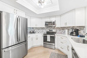 A modern kitchen with stainless steel appliances, white cabinetry, and a tiled backsplash. - Ocean View Retreat at Beach Palms (Indian Shores)