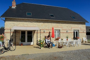 A stone building with a black roof, a covered patio with outdoor seating, and a bicycle parked outside.