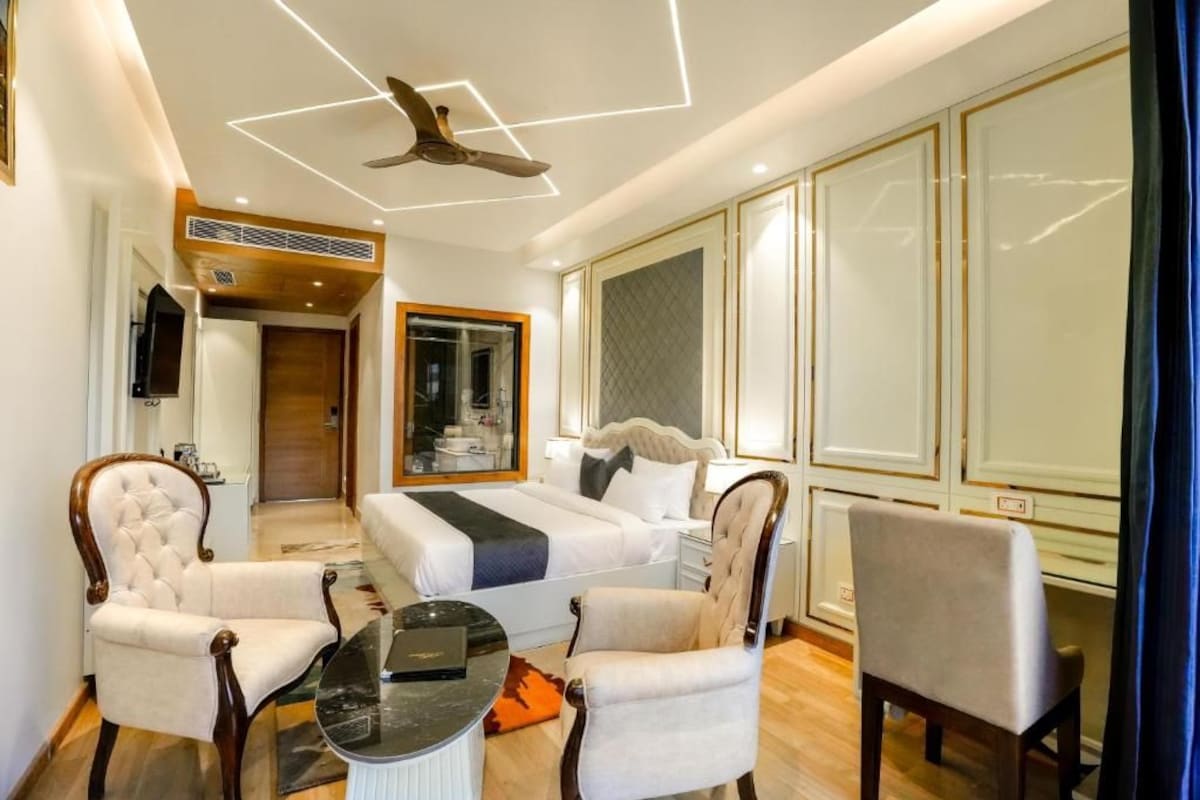 Habitación de hotel con cama, dos sillones, una mesita, ventilador de techo y televisor.