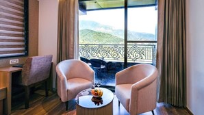 A hotel room with a balcony, two armchairs, a small table with a fruit bowl and glasses, and a view of mountains. - Alivaa Hotel, Mcleodganj With Best Dhauladhar View (Dharamshala)