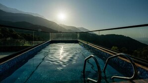 Piscina ao ar livre com vista para montanhas e o sol.