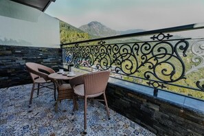 A balcony with wicker chairs and a table, a patterned floor, and a view of mountains. - Alivaa Hotel, Mcleodganj With Best Dhauladhar View (Dharamshala)