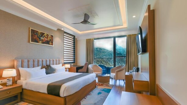 Quarto de hotel com uma cama grande, uma escrivaninha, uma cadeira, televisão e varanda com vista.