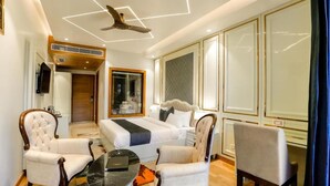 Quarto de hotel com uma cama, duas poltronas, uma mesinha, um ventilador de teto e uma televisão.