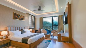 A hotel room with a large bed, a desk, a chair, a TV, and a balcony with a view. - Alivaa Hotel, Mcleodganj With Best Dhauladhar View (Dharamshala)