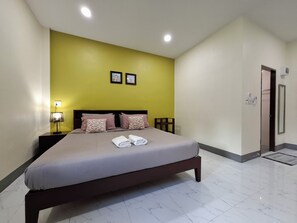 A hotel room with a bed, a nightstand, a wall-mounted lamp, and a door.
