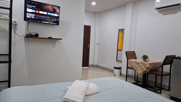 A hotel room with a bed, a television mounted on the wall, a small table with chairs, and an air conditioning unit.