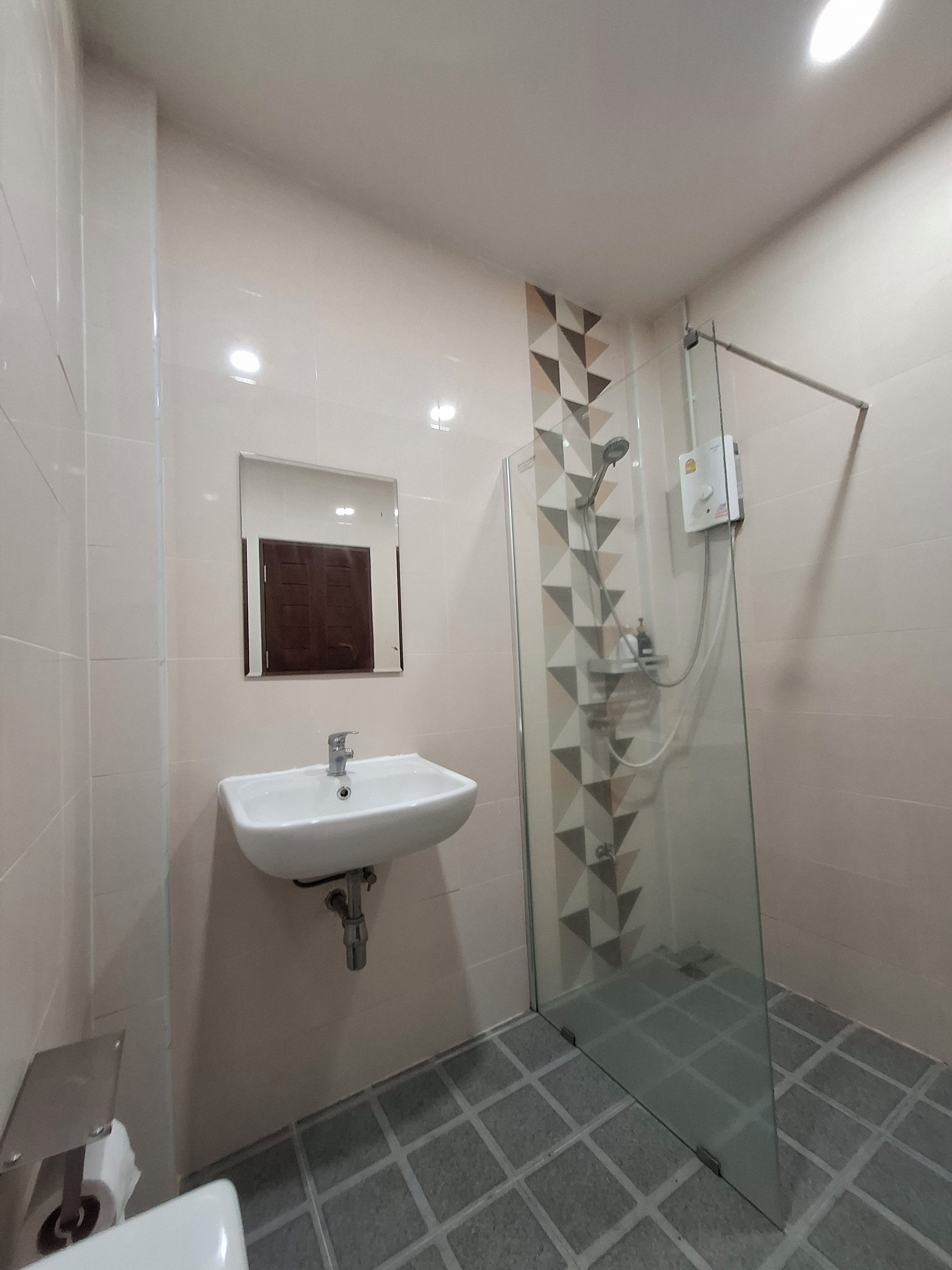 Un baño con cabina de ducha de vidrio, lavamanos blanco y suelo de baldosas.