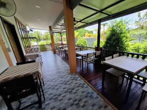 An outdoor patio with tables and chairs, a covered walkway, and a view of greenery.