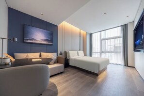 Quarto de hotel moderno com cama, sofá, escrivaninha e uma grande janela.