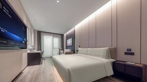 Una habitación de hotel moderna con una cama grande, un escritorio, una silla, un televisor montado en la pared y una mesita de noche.