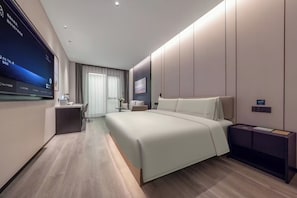 A modern hotel room with a large bed, a desk, a chair, a TV mounted on the wall, and a bedside table.