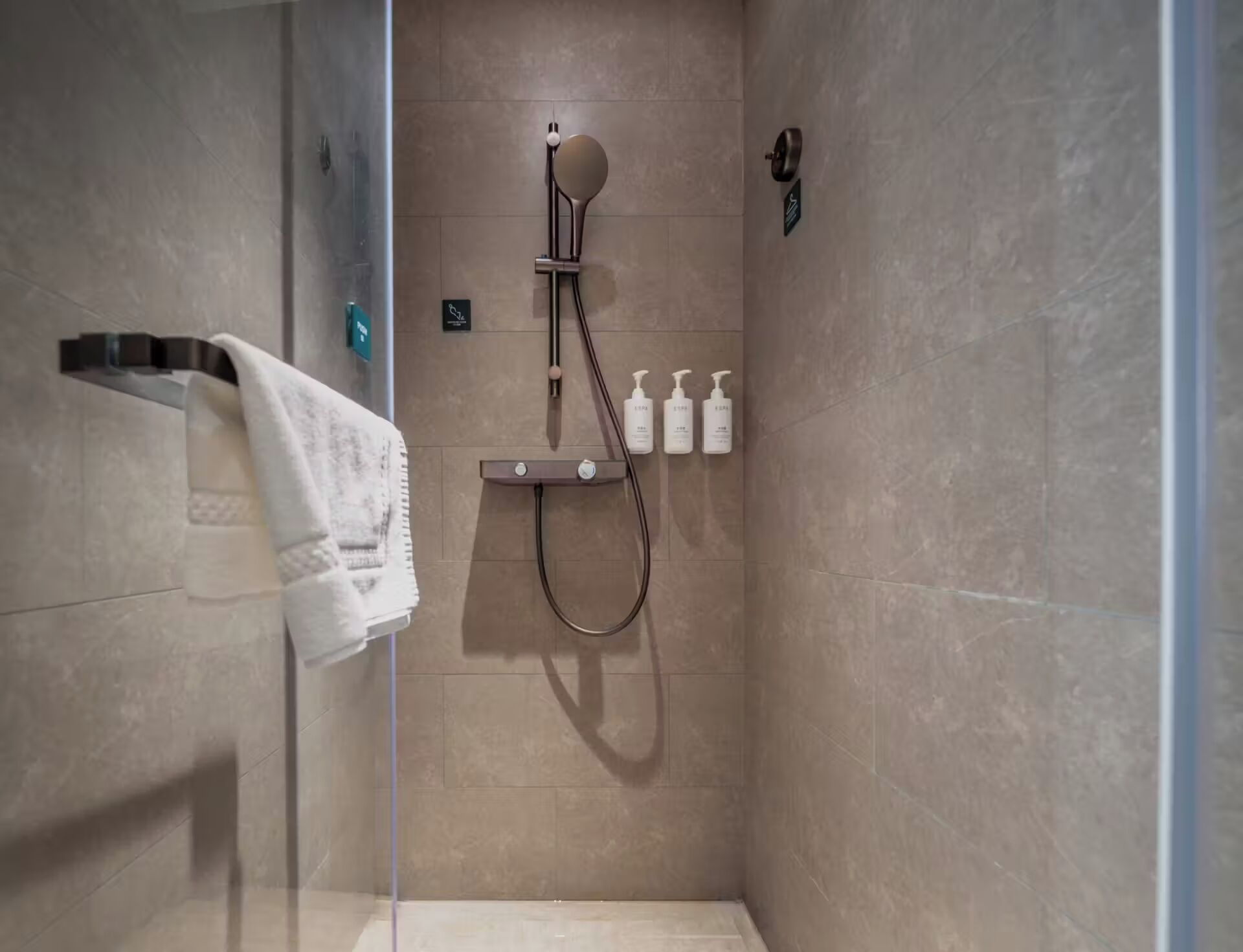 A modern shower with a handheld showerhead, a towel rack, and a set of toiletries on the wall.