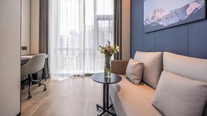 Habitación de hotel moderna con sofá, escritorio y vistas a la ciudad a través de cortinas traslúcidas.