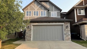 A residential house with a garage, stone exterior, and a tree in the front yard. - Mountain View Retreat w/ Fireplace in Aspen Hills (Calgary)