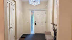 A hallway with a door, a mat, a bench, and a chandelier. - Mountain View Retreat w/ Fireplace in Aspen Hills (Calgary)