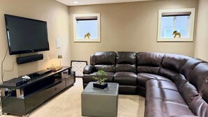 A living room with a large flat-screen TV, a leather sofa, a coffee table, and two framed pictures on the wall.