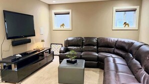 A living room with a large flat-screen TV, a leather sofa, a coffee table, and two framed pictures on the wall.