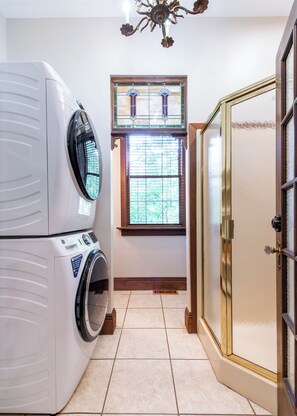 Une buanderie équipée d’une machine à laver et d’un sèche-linge superposés, d’une fenêtre avec des stores et d’une porte dotée d’un panneau en verre.