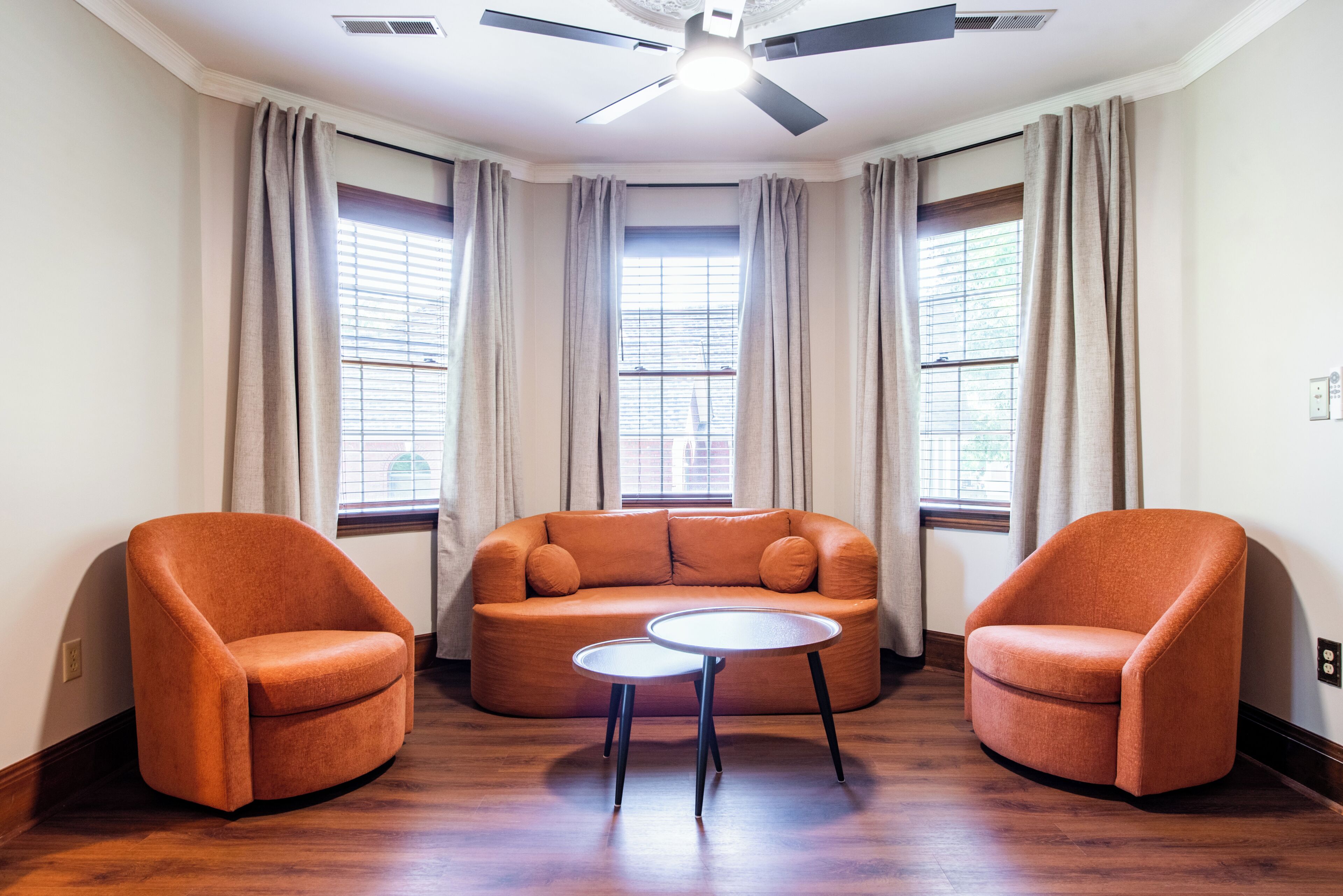 Une pièce avec un canapé orange aux formes arrondies, deux fauteuils assortis, une petite table ronde et un ventilateur de plafond.
