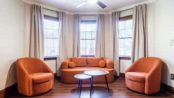 A room with a curved orange sofa, two matching armchairs, a small round table, and a ceiling fan.