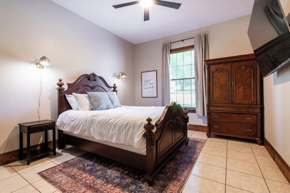 Une chambre à coucher comprenant un lit, une table de chevet, une commode et un ventilateur de plafond.