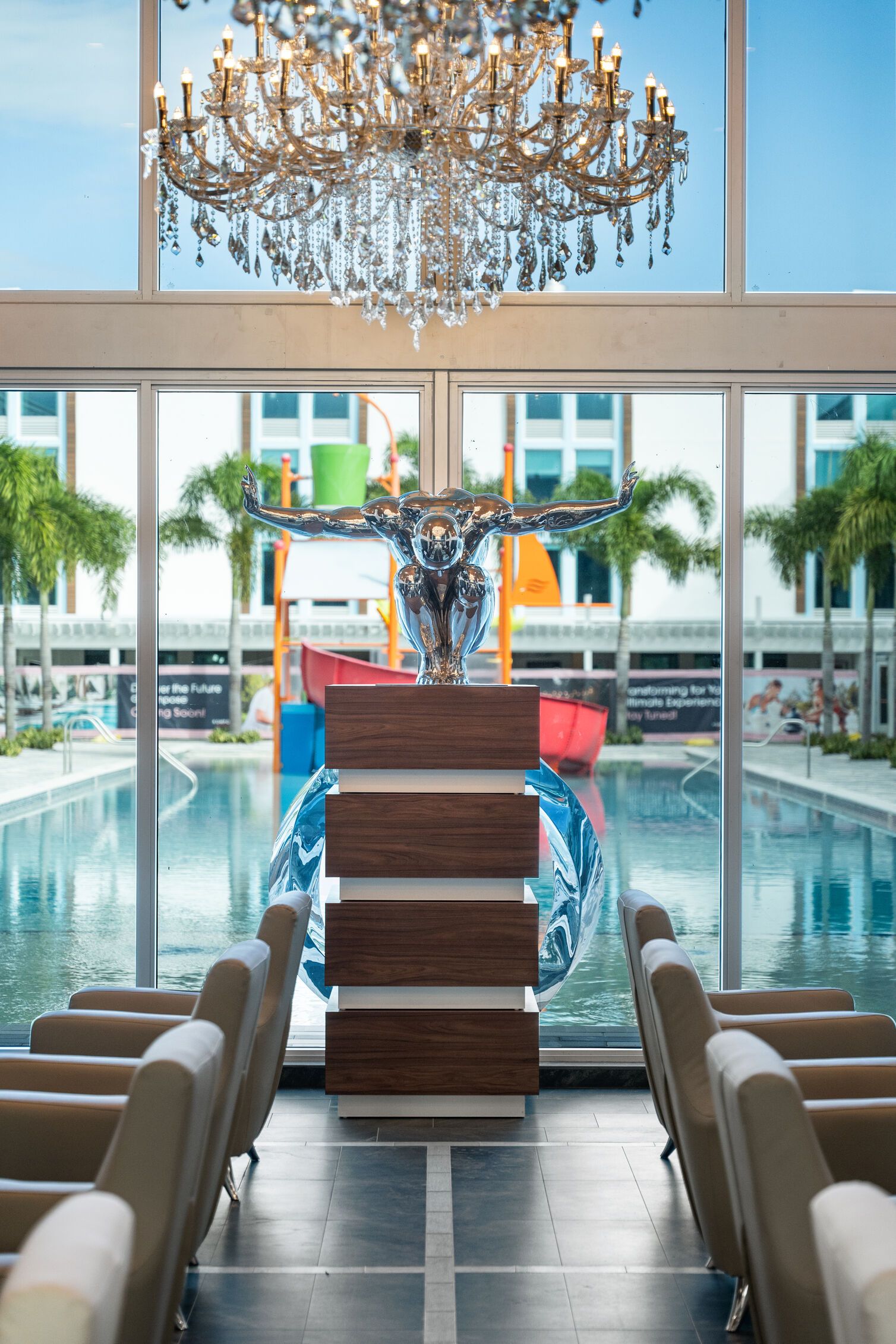A poolside area with a large chandelier, a decorative sculpture, and a view of a building with palm trees.